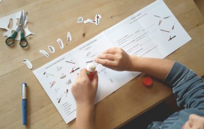 Kindergartenkind bastelt mit Papier und Kleber auf Holztisch