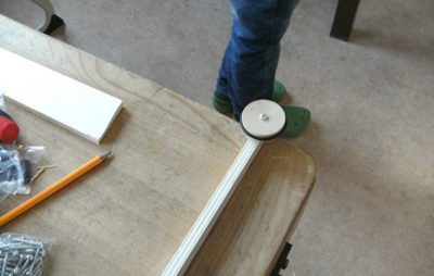 Person montiert Tischbein mit Rad an Holztisch