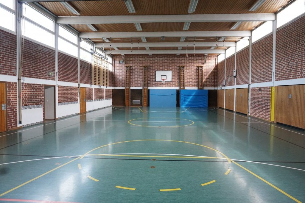 Leere Schulsporthalle mit Basketballkorb und Holzwänden