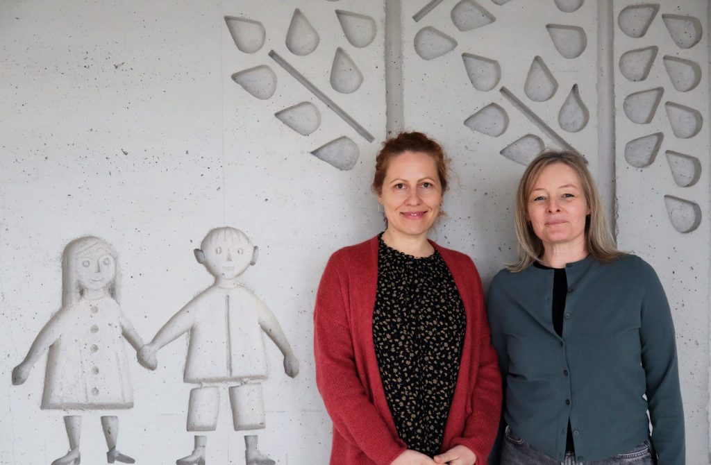 Jugendsozialarbeit, Zwei lächelnde Frauen stehen vor Kunstwand im Raum. Christiane Wünsch-Brändle, Gerlinde Wild